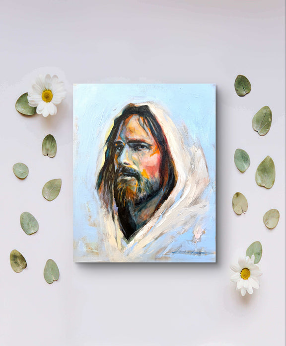 A high quality print depicting jesus full of grace and compassion by a real artist. The print is laying on a table with flowers and leaves.  