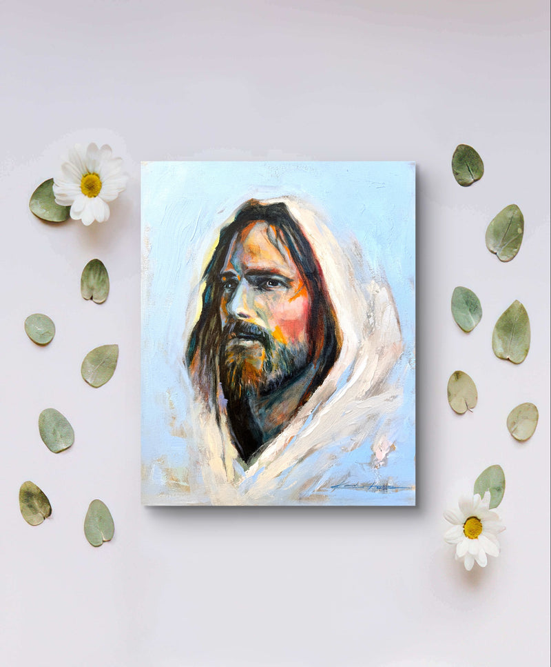 A high quality print depicting jesus full of grace and compassion by a real artist. The print is laying on a table with flowers and leaves.  