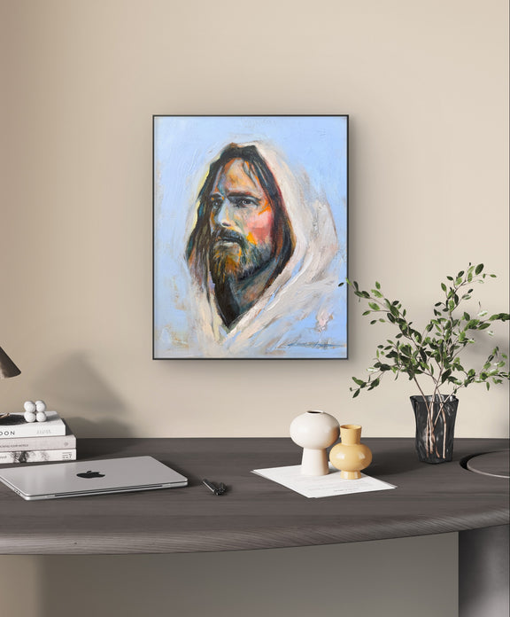Black framed Original Oil Painting, a portrait of Jesus with big brushstrokes and thick paint, a lot of texture and vibrant colors in an office hanging on the wall over a desk with a small olive plant. 